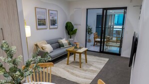 Ein Wohnzimmer mit Sofa, Couchtisch und Sesseln, ein Esstisch mit Blumenvase und eine Glasschiebetür, die auf einen Balkon führt.