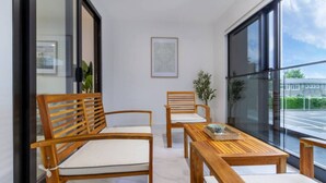 Ein modernes Zimmer mit Holzmöbeln, darunter zwei Stühle und ein Tisch, ein gerahmtes Bild an der Wand und ein Blick ins Freie durch große Fenster.