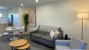 A modern living room with a grey sofa, a grey armchair, a round coffee table, and a dining area with a white table and chairs.