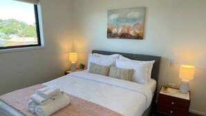 A neatly made bed with a pink blanket and white towels, two bedside lamps, and a painting on the wall.