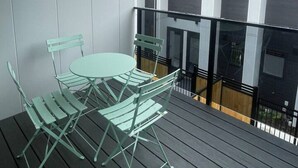 A balcony with a round table and four chairs, a railing, and a building with large windows in the background. - Peaceful Inner-City Studio – Bath Street (Christchurch)