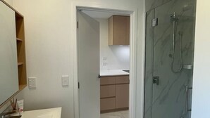 A modern bathroom with a glass-enclosed shower, a white sink, and wooden cabinets. - Peaceful Inner-City Studio – Bath Street (Christchurch)