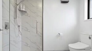 Une salle de bain moderne dotée d’une douche à parois de verre, de toilettes et d’un purificateur d’air fixé au mur.