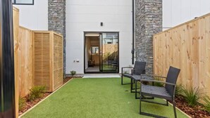Une maison moderne avec une façade en pierre, une clôture en bois et un petit patio agrémenté d’une table et de chaises.