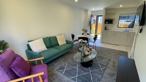 En stue med en grøn sofa, en lilla lænestol og et sofabord med blomster.