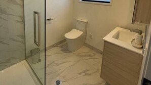 Et badeværelse med brusekabine i glas, toilet, vask og et vindue.