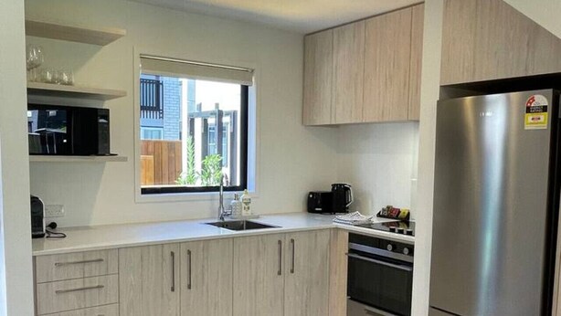 A modern kitchen with light wood cabinets, a stainless steel refrigerator, and a window providing natural light.