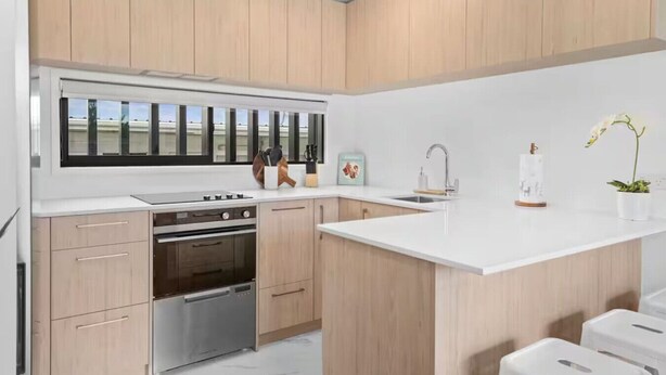 A modern kitchen with wooden cabinets, stainless steel appliances, a large window, and a white countertop. - Beautiful Bay of Plenty 2 Bed (Tauranga)
