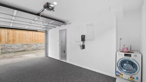 A clean, modern laundry room with a washing machine, a dryer, and a security camera. - Stunning Bay of Plenty 2 Bed (Tauranga)