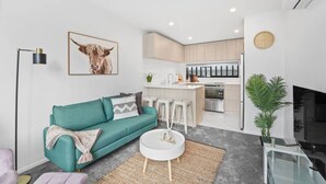 A modern living room with a teal sofa, a coffee table, and a kitchen area with a bar. - Stylish Tauranga Home (Tauranga)