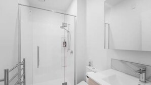 Een moderne badkamer met een glazen douchecabine, een witte wastafel met een marmeren blad en een grote spiegel erboven.