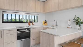 A modern kitchen with light wood cabinets, a large window, a built-in oven, a sink, and bar stools.