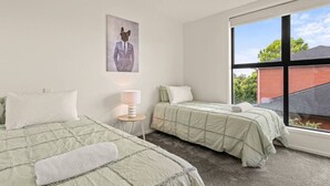 Una camera da letto con due letti, una finestra che si affaccia su un edificio in mattoni e un quadro raffigurante un cane in abito.