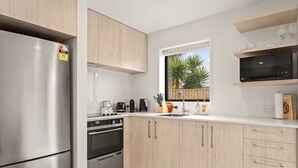 A modern kitchen with stainless steel appliances, wooden cabinets, and a window with a view of palm trees. - Vibrant 2 bed Henderson Abode (Auckland)