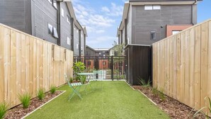 A courtyard with artificial grass, a metal gate, and a small table with chairs. - Vibrant 2 bed Henderson Abode (Auckland)