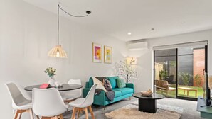 En moderne stue med en teal farvet sofa, hvide stole, et rundt spisebord og en stor skydedør, der fører til en baghave.