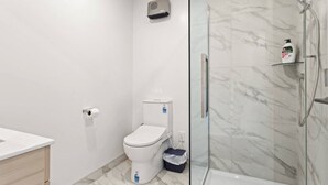 A modern bathroom with a toilet, a shower enclosure, and a marble-tiled wall. - Well-styled Vibrant 2 Bed Home (Auckland)