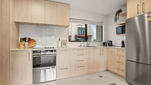 A modern kitchen with light wood cabinets, stainless steel appliances, and a large window. - Well-styled Vibrant 2 Bed Home (Auckland)