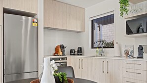A modern kitchen with stainless steel appliances, light wood cabinets, and a dining area with a black table. - Central Auckland Townhouse (Auckland)