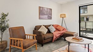 Un salon avec un canapé en cuir marron, un fauteuil en bois, une lampe sur pied et une petite table sur laquelle repose un livre.
