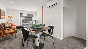 Un salon moderne avec une table de salle à manger ronde, des chaises noires, un canapé marron et une grande fenêtre.