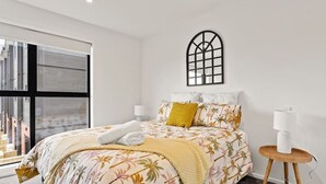 Ein modernes Schlafzimmer mit einem großen Bett, einem Fenster mit Aussicht, einem wandmontierten Bogenfenster und einem Nachttisch mit Lampe.
