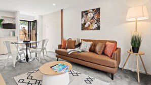 Un salon moderne avec un canapé en cuir marron, une table basse ronde et un coin repas comprenant une table et des chaises blanches.