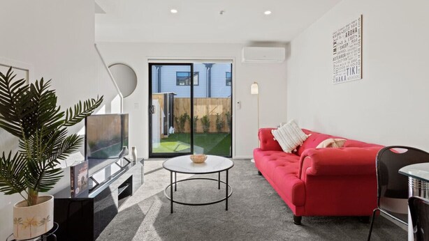 A modern living room with a red sofa, a round coffee table, and a TV. There is a sliding glass door leading to a backyard.