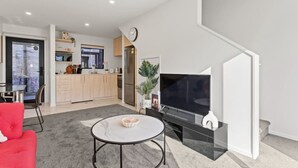 A modern living room with a flat-screen TV, a red sofa, and a kitchen area with wooden cabinets and a refrigerator.