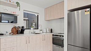 A modern kitchen with light wood cabinets, stainless steel appliances, and a window providing natural light.