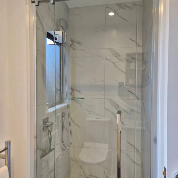 Une douche fermée par des parois en verre, dotée d’un pommeau de douche à main et d’un robinet mural.