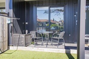 An outdoor patio with a table and chairs, a wooden fence, and a glass door leading to a building. - Cozy Studio on Macky Street (Lower Hutt)