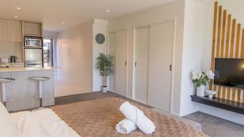 Een moderne hotelkamer met een bed, een televisie, een kitchenette en een schuifdeurkast.