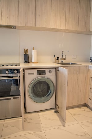 A compact kitchen with a built-in washer, oven, and sink. - Cozy Studio on Macky Street (Lower Hutt)