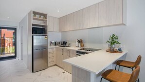 A modern kitchen with a built-in refrigerator, a stove, and a sink. There are two bar stools and a potted plant on the counter. - Serene Escape: Studio in Macky Street (Lower Hutt)