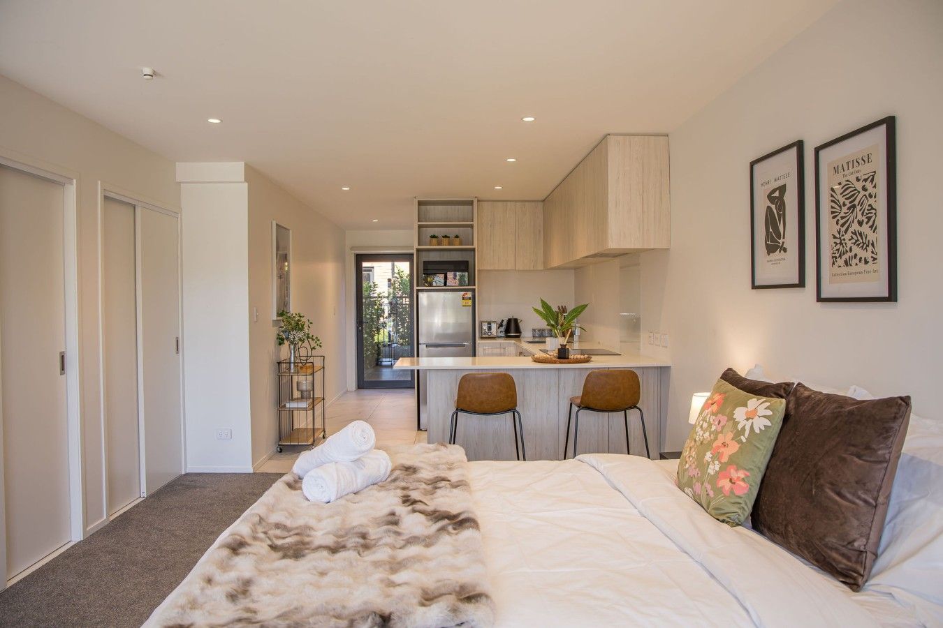 A bedroom with a large bed, a small kitchenette, and a view of the outside.