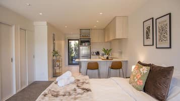 A bedroom with a large bed, a small kitchenette, and a view of the outside.