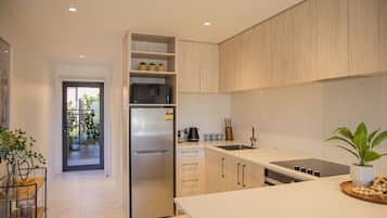 Et moderne køkken med indbygget køleskab, vask og komfur. Der står en plante på bordet, og en dør fører ud til en balkon.