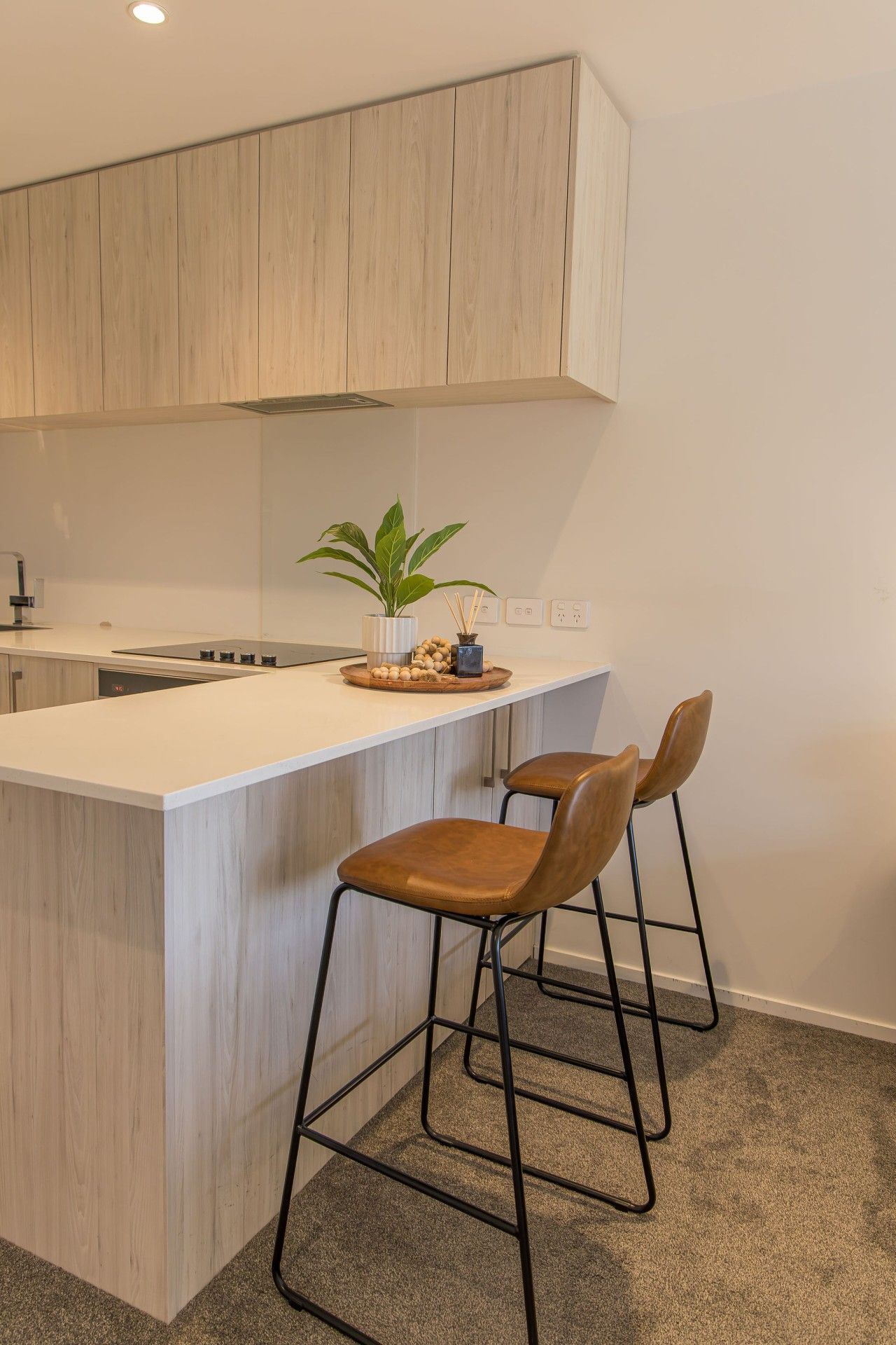 A modern kitchen with a central island, bar stools, and a potted plant.