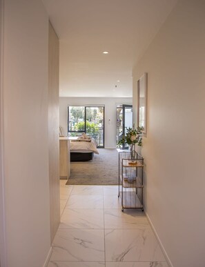 A hallway with a bed, a small table with a vase, and a view of a balcony. - Serene Escape: Studio in Macky Street (Lower Hutt)