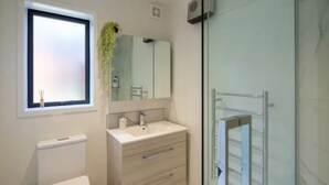 A modern bathroom with a toilet, sink, and glass shower enclosure. - Serene Escape: Studio in Macky Street (Lower Hutt)