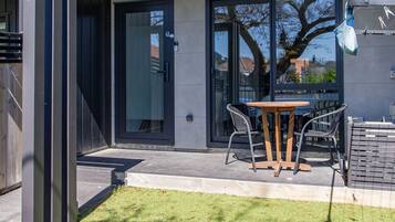 A modern building with a glass door entrance, a small outdoor seating area with a table and chairs, and a grassy lawn.
