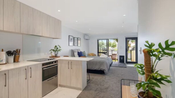 A modern kitchen with light wood cabinets, a central island, and a dining area. - Serene Escape: Studio in Macky Street (Lower Hutt)