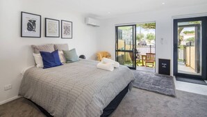 A bedroom with a large bed, a balcony with a chair, and three framed artworks on the wall. - Serene Escape: Studio in Macky Street (Lower Hutt)