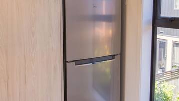 A compact kitchen with a built-in stainless steel refrigerator, a window with a view of the outside, and a wooden cabinet above the fridge.