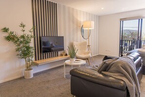 Ein modernes Wohnzimmer mit Fernseher, Topfpflanze, Sofa und Sessel.