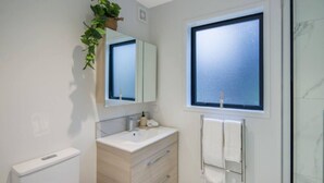 A modern bathroom with a white vanity, a mirror, a window, and a towel rack. - Bright Studio Apartment on Macky Street (Lower Hutt)