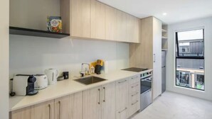 A modern kitchen with light wood cabinets, a built-in oven, and a large window offering a view of the city. - Bright Studio Apartment on Macky Street (Lower Hutt)