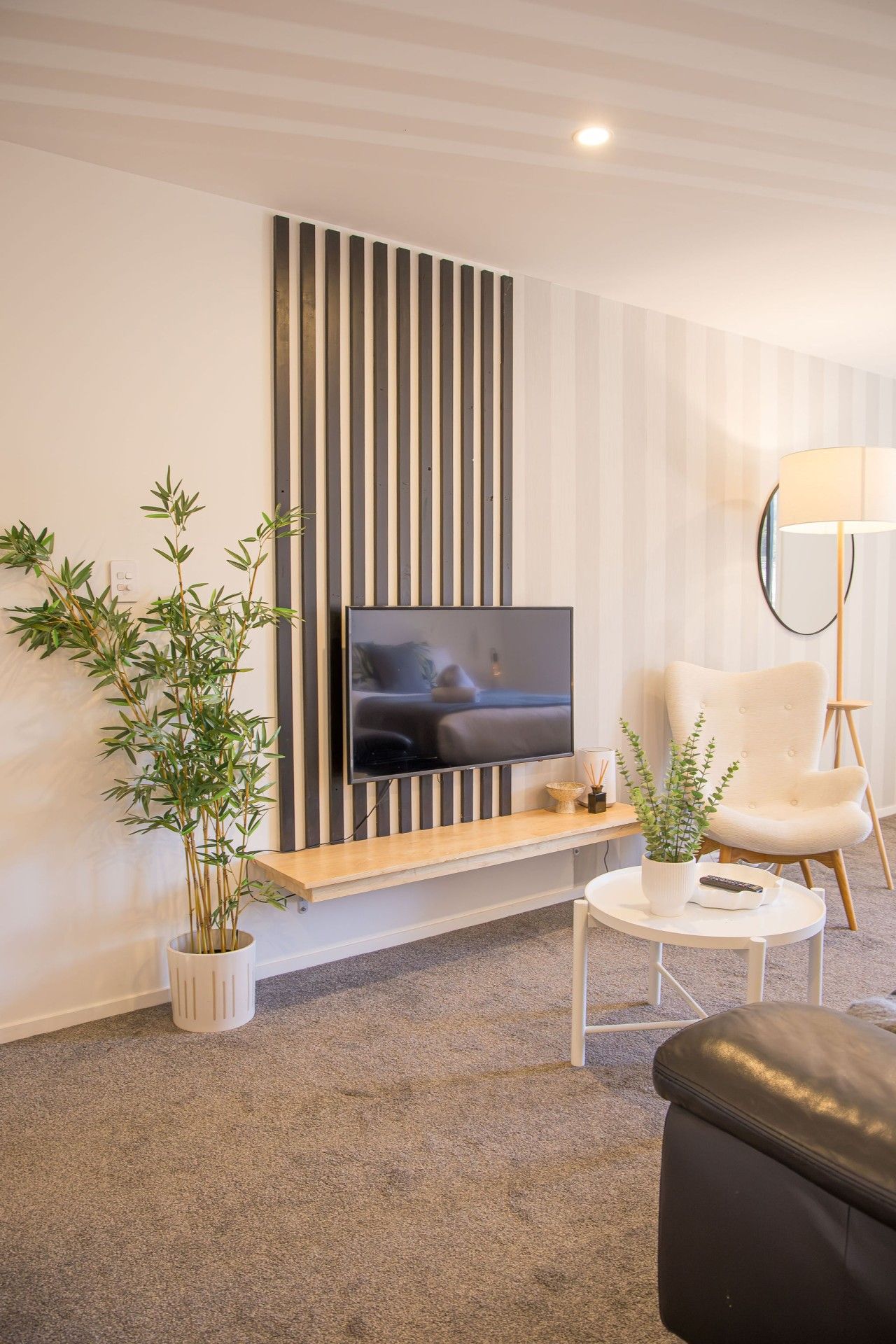 A modern living room with a flat-screen TV mounted on a wall, a white armchair, a round coffee table, and a potted plant.