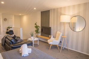 Ein modernes Wohnzimmer mit einer Couch, einem Fernseher, einem Couchtisch, einem Sessel und einer Stehlampe.